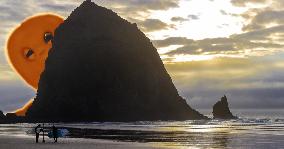 Horace, a big orange fuzzy monster, peeks out from behind Haystack Rock at sunset while two surfers stand on the wet sand with their boards